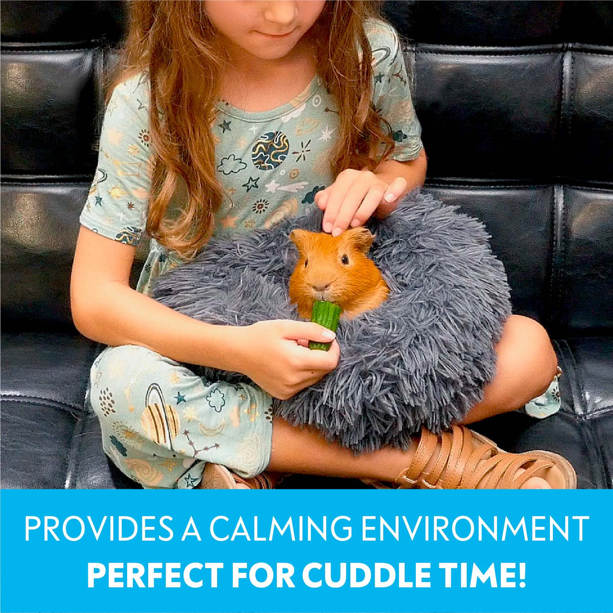 A young child holding a guinea pig inside a dark grey Paw Inspired Furr-O bed on her lap while feeding it a cucumber slice.