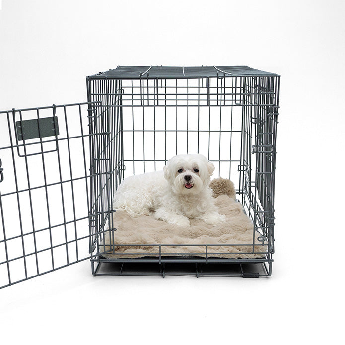 A white dog lying on a Paw Inspired tan waterproof blanket inside a metal pet crate.